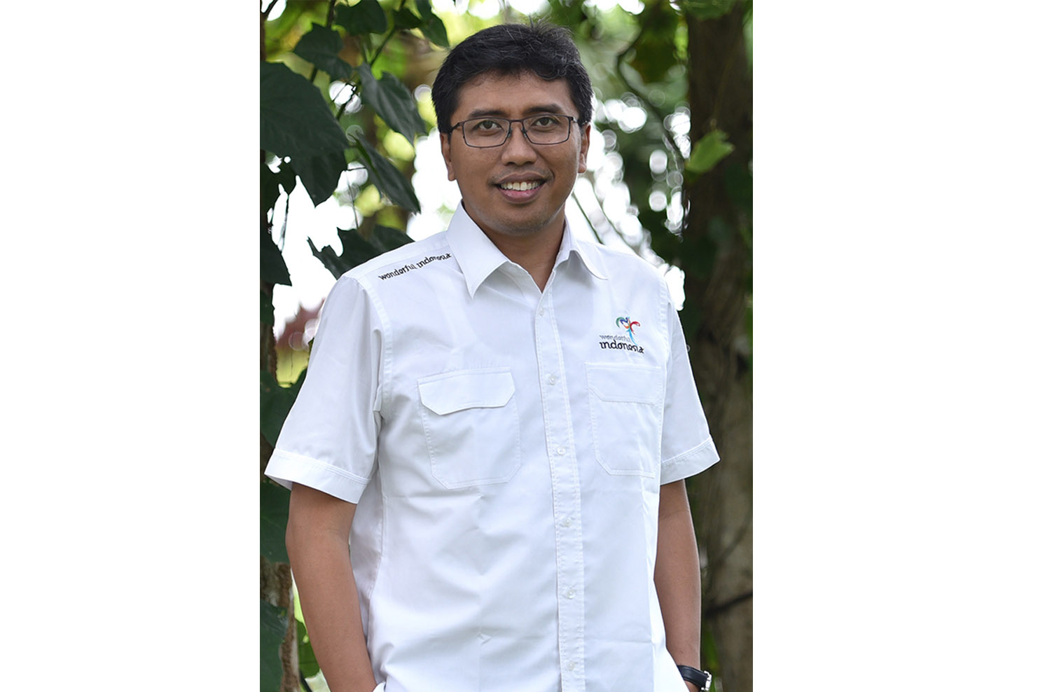 A man with glasses wearing a white shirt with wonderful Indonesia logo on the chest